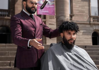 Mansoor wird die Haarschneidemaschine von einer Hand in die andere während er seinem Kunden die Haare schneidet